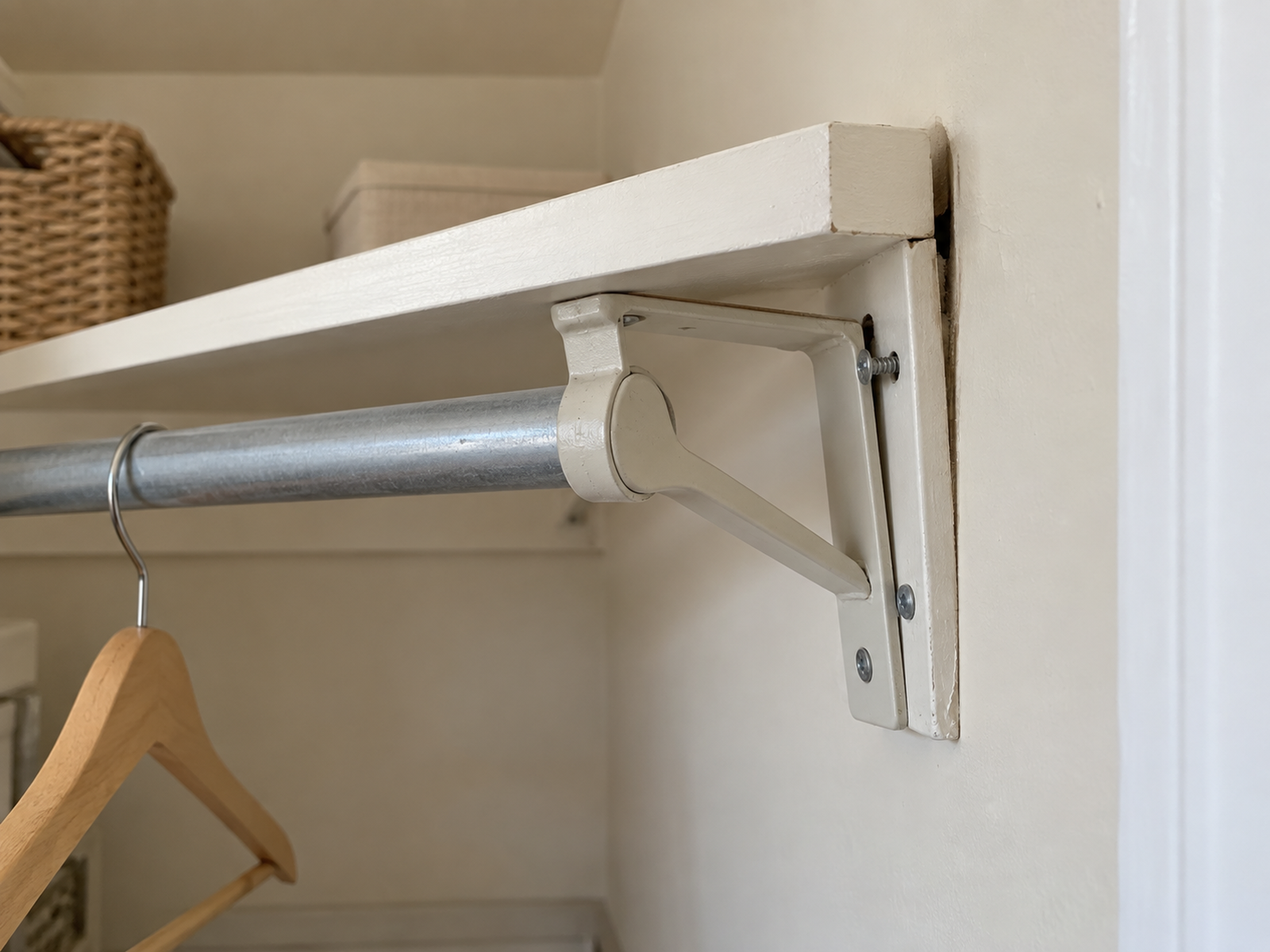An almost unloaded closet rod ends at a shelf bracket pulling away from the wall, with a narrow gap and one backed-out screw visible.