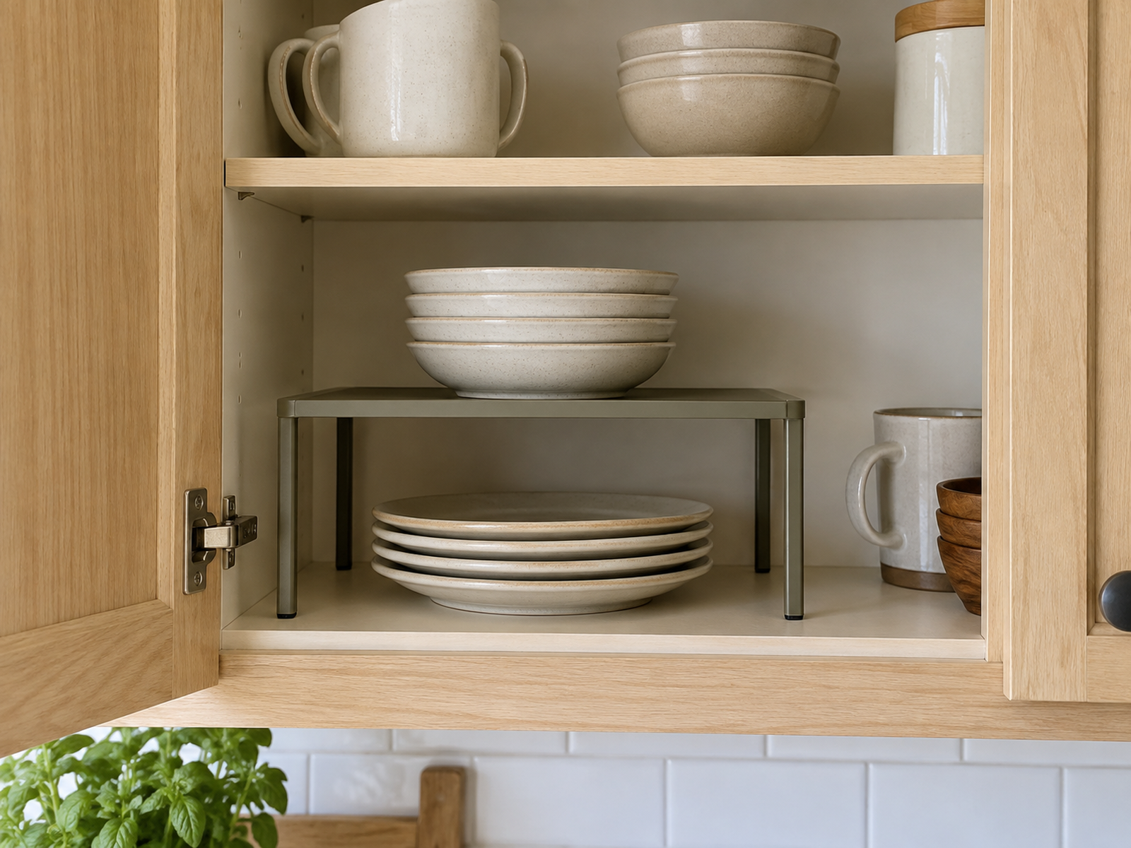 A freestanding shelf riser creates separate accessible levels for a short plate stack below and shallow bowls above inside a compact kitchen cabinet.